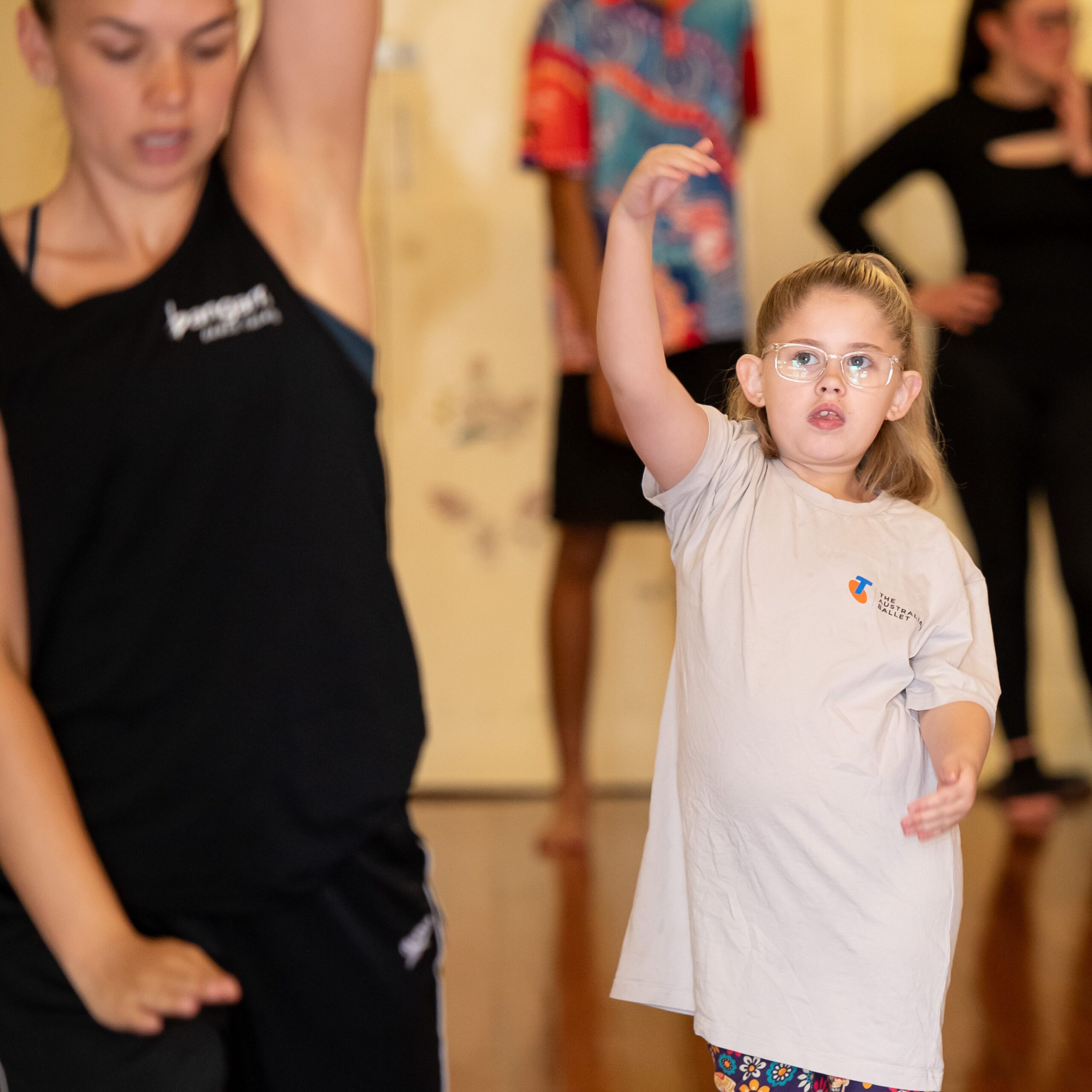 Photo of a young girl concentrating as she copies dance moves from an instructor in front of her.