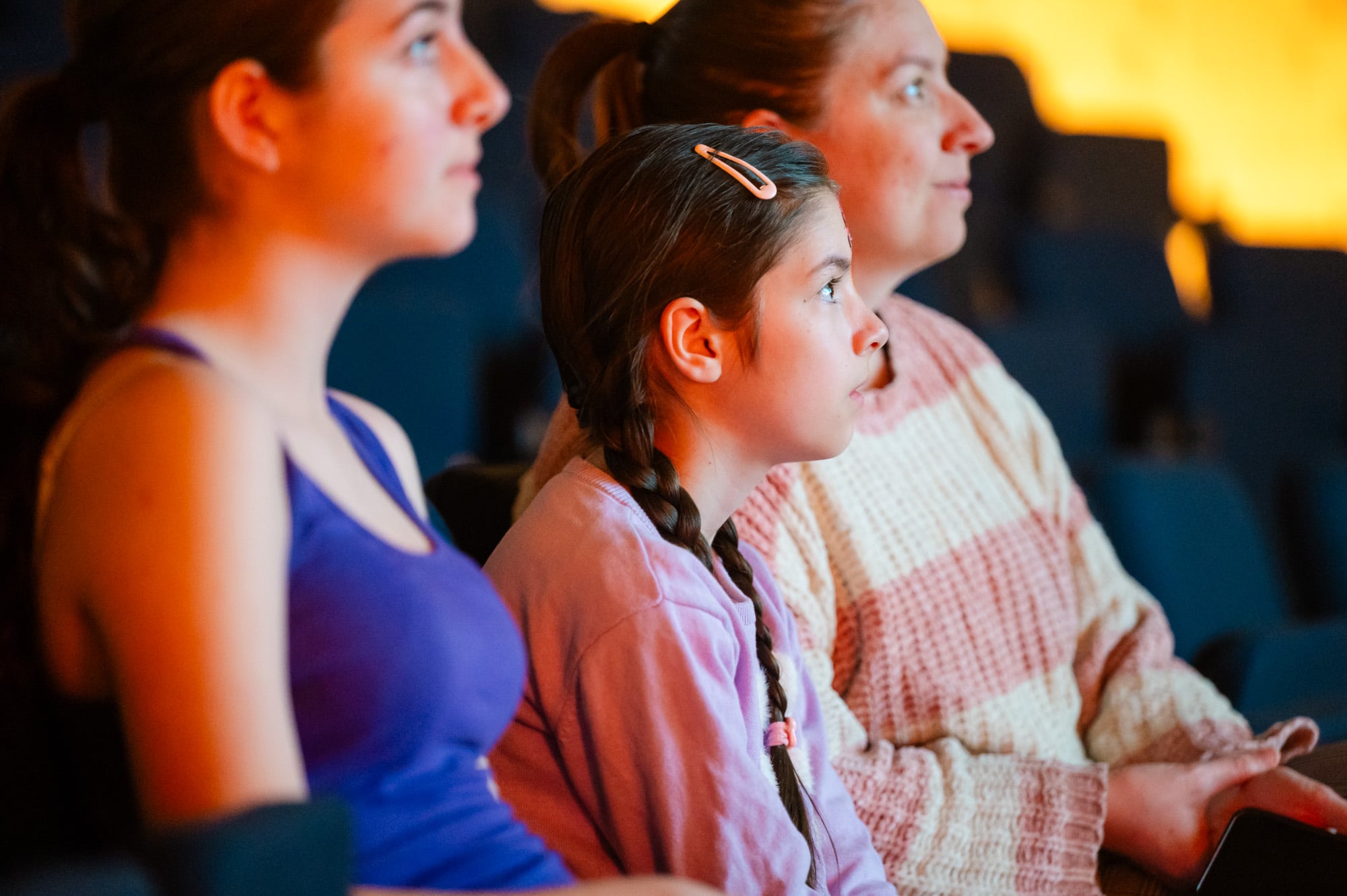 Young girl and two women in a theatre watching a performance.